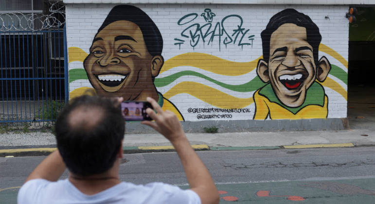 Torcedor tira foto de mural com as caricaturas de Pelé e Garrincha, no Rio de Janeiro