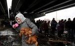 Mulher carrega cachorro enquanto cruza uma ponte destruída na cidade de Irpin, a noroeste de Kiev