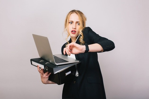 Mulher jovem segura nas mãos dois fichários e um notebook, enquanto corre contra o tempo no trabalho. Lookstudio / Freepik