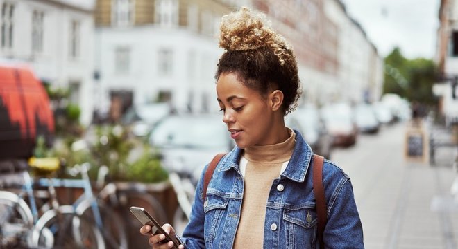 Mulher na rua olha sorrindo para celular