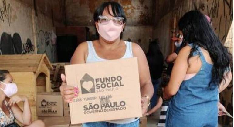 Mulher recebe cesta básica durante entrega da ONG em comunidade da zona oeste de SP