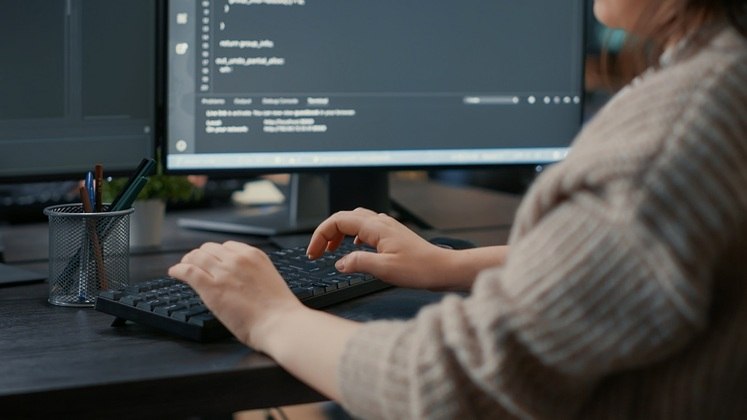 Mulher ruiva programadora escreve código em um desktop. Freepik - DCStudio