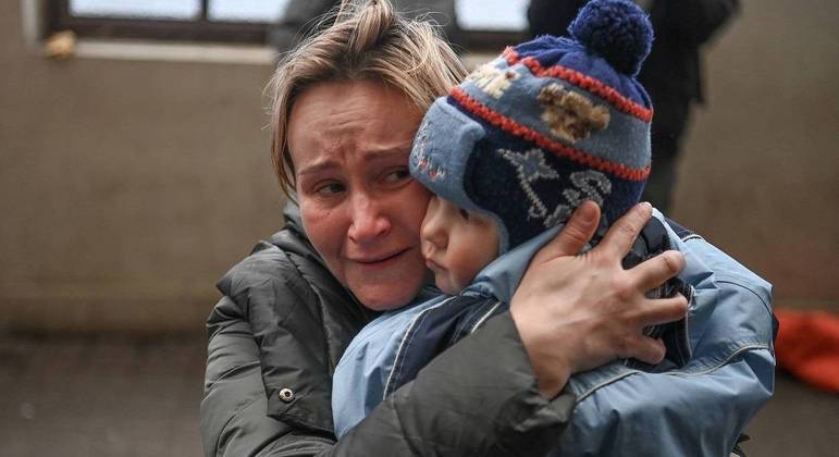 Mulher segura criança enquanto aguarda embarque em trem para se refugiar na Polônia