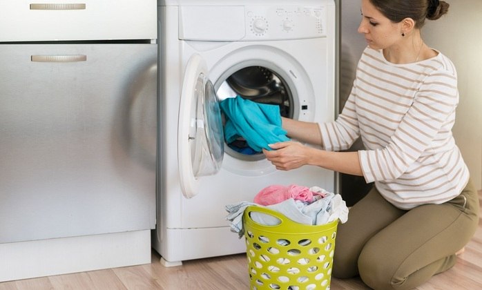 Mulher tira roupas da máquina de lavar com abertura frontal. Freepik