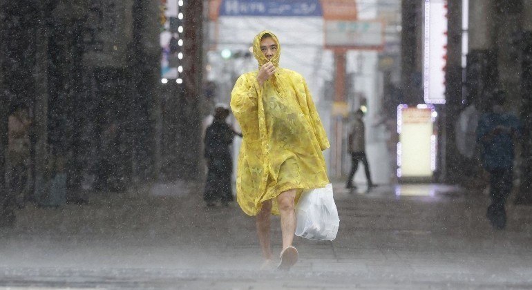 com fortes chuvas e ventos, homem usa capa de chuva em rua de Kyushu
