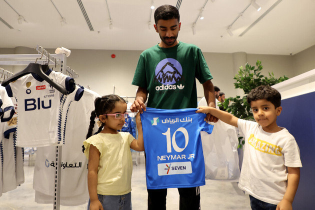 Homem ao lado de duas crianças posa com a camisa do jogador, que se soma a outros craques que brilhavam no continente europeu e que foram seduzidos pelas altas cifras sauditas, como CR7, Benzema e Firmino