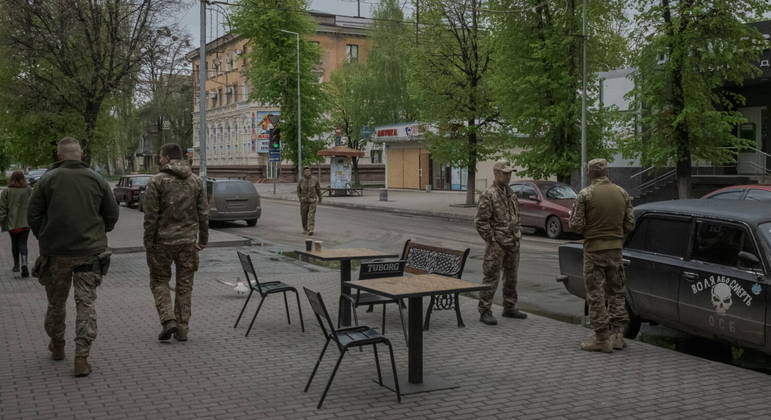 Soldados ucranianos conversam perto de um café no centro de Slovyansk, na Ucrânia. Enquanto vagam pela cidade destruída, é comum que os adolescentes cruzem com soldados prontos para o combate, armados com fuzil
