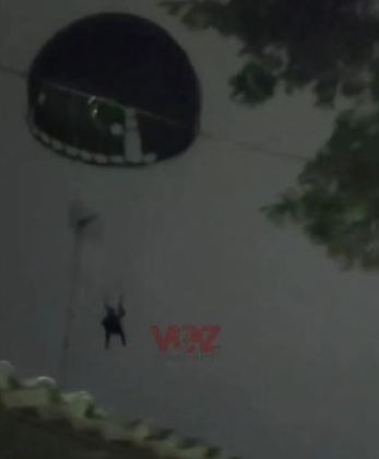 O paraquedista ainda passa rente à fiação da rede elétrica, diante de moradores apavorados com a cena. 