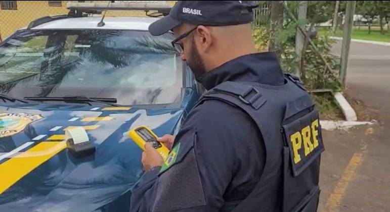 Agente da Polícia Rodoviária Federal realizando teste do bafômetro em operação

