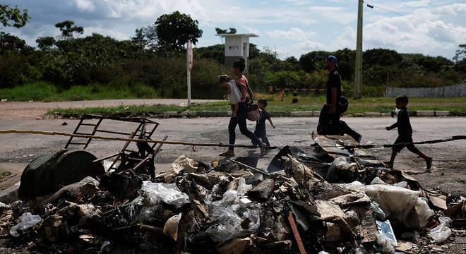 Venezuelanos caminham em frente a pertences destruídos após ataque de brasileiros em Pacaraima