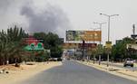 Paisagem da cidade de Cartum, no Sudão, com fumaça ao fundo e um carro, em uma rua quase deserta. AFP – 16/04/2023