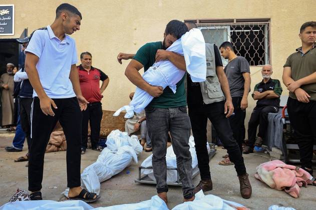 Subiu para 6.051 neste domingo (22) o número de mortos na guerra entre o Exército de Israel e o grupo terrorista Hamas. O Ministério da Saúde palestino informou que o número de mortos na Faixa de Gaza aumentou para 4.651 vítimas. Na foto, um homem palestino chora ao carregar o corpo do filho enrolado em um lençol, em frente ao necrotério do hospital Al-Aqsa, em Deir Balah, no centro da Faixa de Gaza