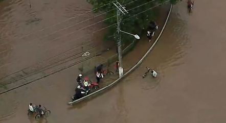 Pedestres e motociclistas atravessam área inundada após chuva em Guarulhos, região metropolitana de São Paulo