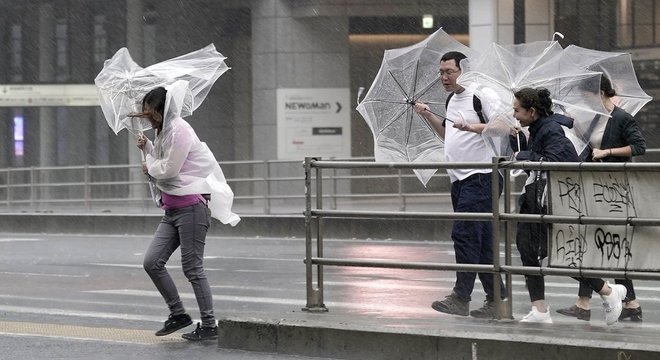 Pedestres têm dificuldade para caminhar por causa de chuva e vento fortes