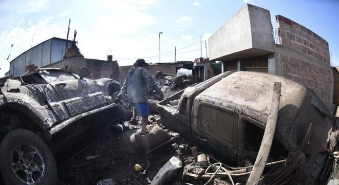 Homem caminha entre casas e carros destruídos por enchente no Peru