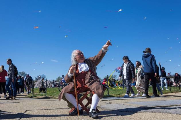 Também tem pipas na capital dos EUA! Barry Stevens, interpretando o personagem de Benjamin Franklin, observa pipas voando no céu durante o Festival de Pipas Cherry Blossoms, em Washington