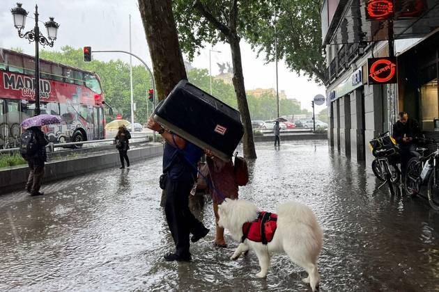 Também na Espanha, um casal se cobre usando um transportador de cães durante forte chuva em Madri