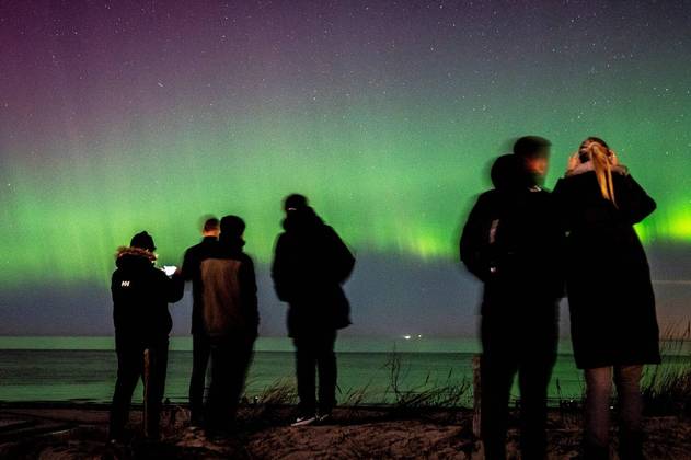 O mundo gira e o planeta continua maluco! E bonito... como mostra a imagem acima, em que pessoas observam o espetáculo da aurora boreal da praia de Hornbaek, na Dinamarca