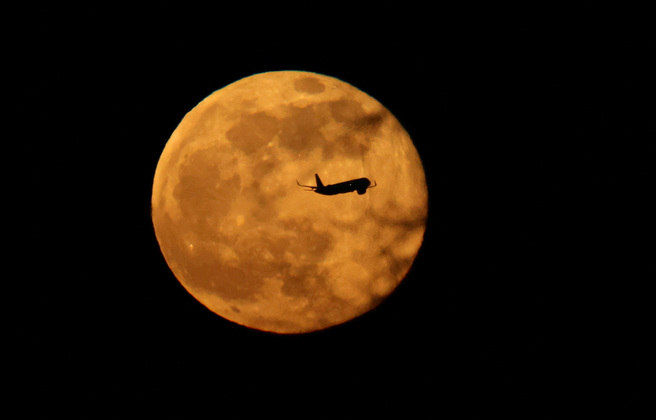 Um avião passa em frente à lua cheia, conhecida como 