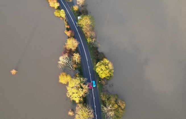 Carros circulam por uma estrada cercada por enchentes, após o rio Arun transbordar. A situação é consequência da passagem de uma tempestade no sul da Grã-Bretanha