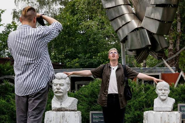 Um homem posa para uma foto estranha com as mãos na cabeça dos líderes soviéticos Lênin e Stálin, em um parque de Moscou, capital da Rússia
