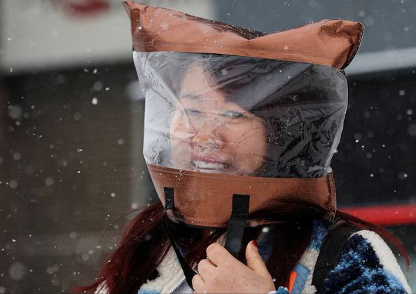 Uma mulher usa um saco plástico para proteger a cabeça em meio a uma nevasca, em Pequim, na China