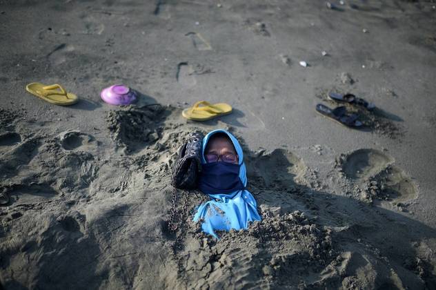 Já na Indonésia, um turista fica coberto com areia preta, que se acredita ter propriedades terapêuticas, durante uma sessão tradicional de tratamento