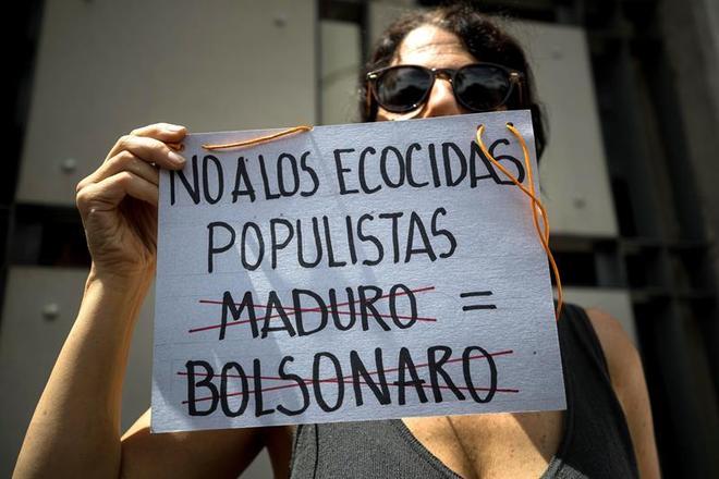 Em Caracas, capital da Venezuela, esta manifestante usou um cartaz para comparar o presidente do Brasil, Jair Bolsonaro, com o venezuelano NicolÃ¡s Maduro. O texto diz 'nÃ£o a ecocidas populistas'