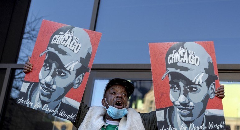 Manifestante segura cartazes com o rosto de Daunte Wright diante do prédio do tribunal
