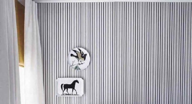 quarto cinza e branco decorado com papel de parede listrado e cabeceira estofada