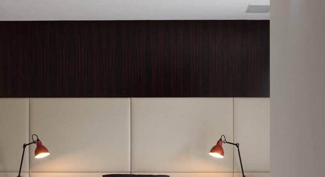 quarto de casal com papel de parede escuro e cabeceira estofada bege