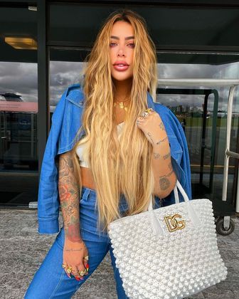 Aqui, ela montou um look casual com calça e jaqueta jeans, Além disso, combinou o top branco com uma bolsa da grife Dolce & Gabanna. Destaque para os acessórios dourados, que conferiram pontos de luz ao visual