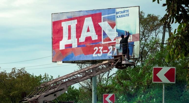Homem coloca placa referente ao referendo russo na Ucrânia onde se lê "sim"
