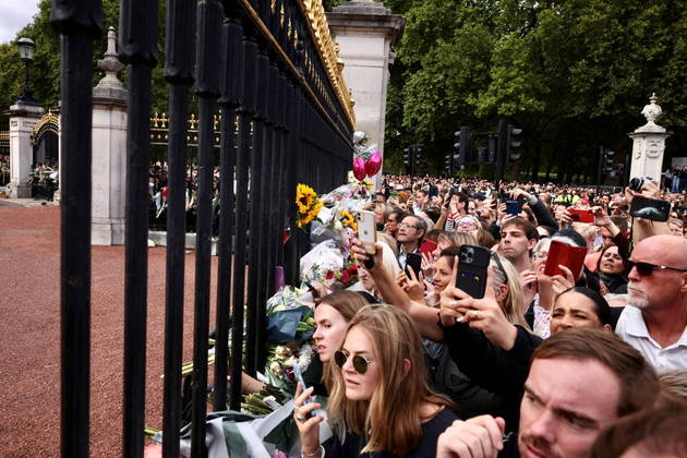 Fãs se espremem nas grades do palácio para fotografar e gravar a chegada de Charles, agora como rei, ao Palácio de Buckingham