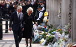 O rei do Reino Unido, Charles 3º, e a rainha consorte, Camilla, caminham perto da grade do Palácio de Buckingham e observam as homenagens que os súditos deixaram para a rainha Elizabeth 2ª, que morreu na última quinta-feira (8)
