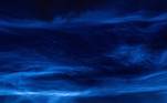 O vapor de água congela nas partículas de poeira e forma cristais de gelo. Assim, quando o sol os ilumina por baixo, esses cristais refletem a luz solar e aparecem como fios azuis elétricos no céu noturno, alcançando a borda do espaço* Sob supervisão de Celso Fonseca 
