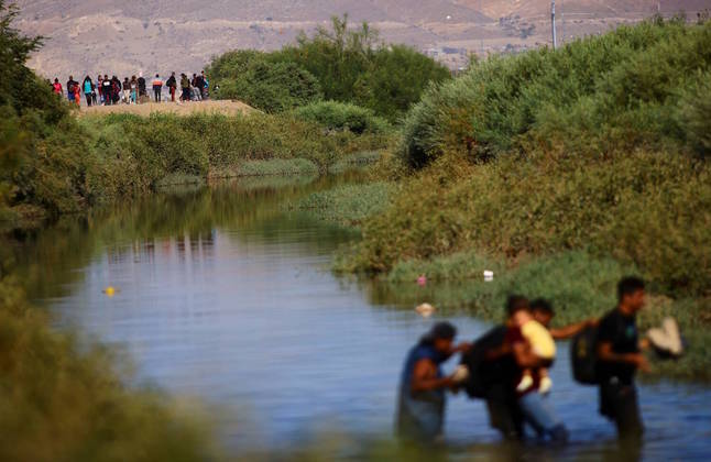 Vários migrantes atravessam o Rio Bravo (chamado de Rio Grande, nos Estados Unidos), que às vezes tem fluxo mais complicado para os estrangeiros. Os migrantes eventualmente carregam seus pertences para o alto, e a água chega ao pescoço de vários deles