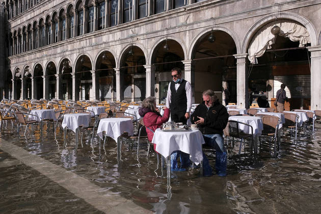People sit at a cafe in a flooded St. Mark's Square during seasonally high water in Venice, Italy November 5, 2021. REUTERS/Manuel Silvestri TPX IMAGES OF THE DAY