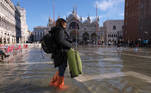 A woman carries a suitcase through a flooded St. Mark's Square during seasonally high water in Venice, Italy November 5, 2021. REUTERS/Manuel Silvestri