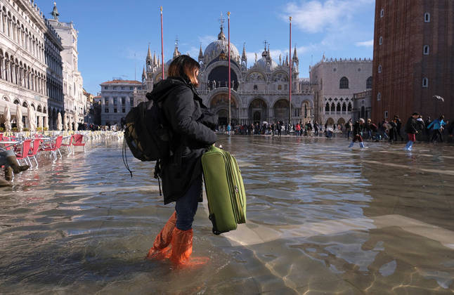 A woman carries a suitcase through a flooded St. Mark's Square during seasonally high water in Venice, Italy November 5, 2021. REUTERS/Manuel Silvestri