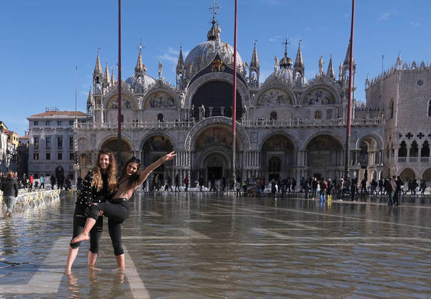 Women pose for a picture in a flooded St. Mark's Square during seasonally high water in Venice, Italy November 5, 2021. REUTERS/Manuel Silvestri