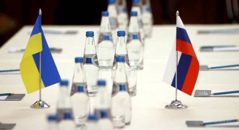 Bandeiras da Ucrânia e da Rússia em uma mesa antes de negociações entre os dois países