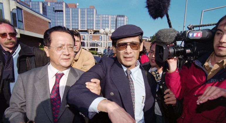 Charles Sobhraj (de boina) e seu advogado saem da corte em Paris, em 1997