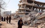 Moradores andam próximos a prédios destruídos pelo terremoto numa busca por sobreviventes em Alepo, neste sábado