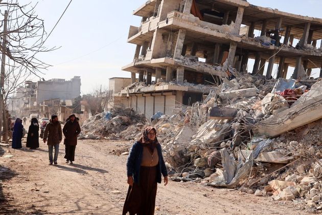 Moradores andam próximos a prédios destruídos pelo terremoto numa busca por sobreviventes em Alepo, neste sábado