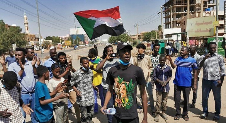 Manifestantes sudanesas levantam bandeiras nacionais e cantam durante um protesto na capital Cartum