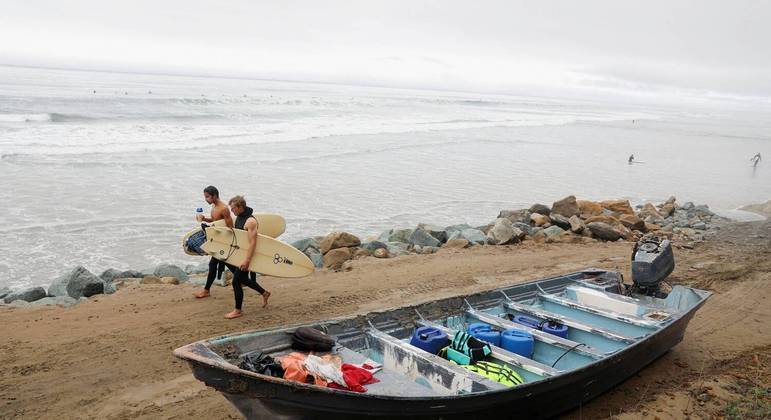 Surfistas caminham ao longo da Black's Beach depois que dois barcos viraram na costa de San Diego