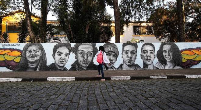Pintura reproduz os rostos das vítimas do massacre sobre o muro branco
