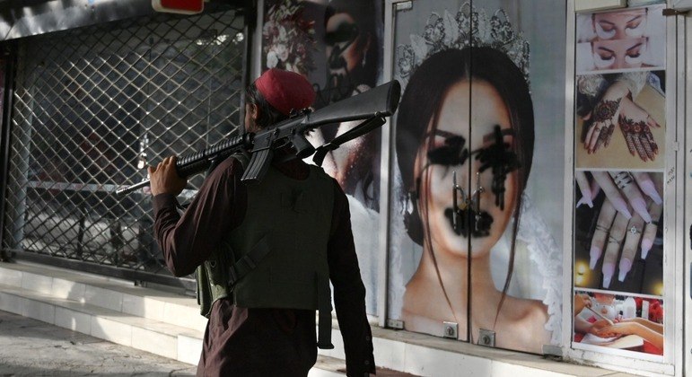 Com rifle no ombro, um talibã fazia patrulha em frente ao estabelecimento