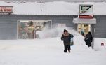 Mulher caminha sobre a neve acumulada em frente a uma loja